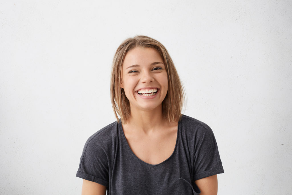 Attractive woman with short fair hair being very glad smiling with broad smile showing her perfect teeth having fun indoors. Joyful excited cheery femlae rejoicing after being proposed to marry dublin braces